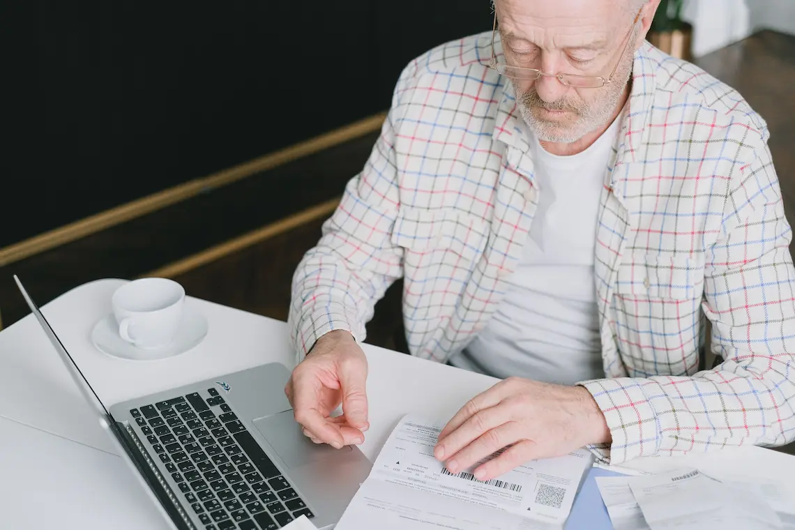 Homem idoso pagando contas no computador, representando autonomia e independência no envelhecimento.